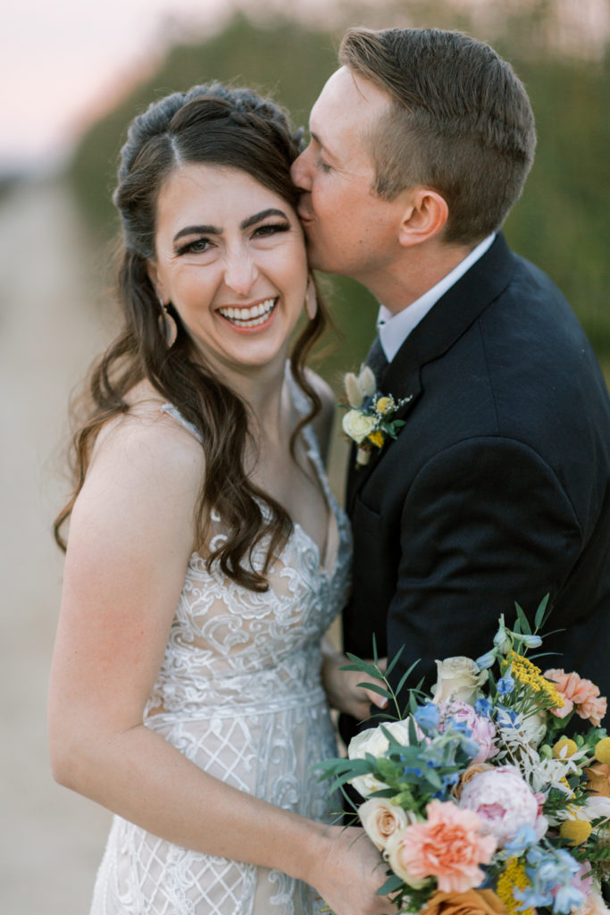 Groom kissing brides head while she laughs.