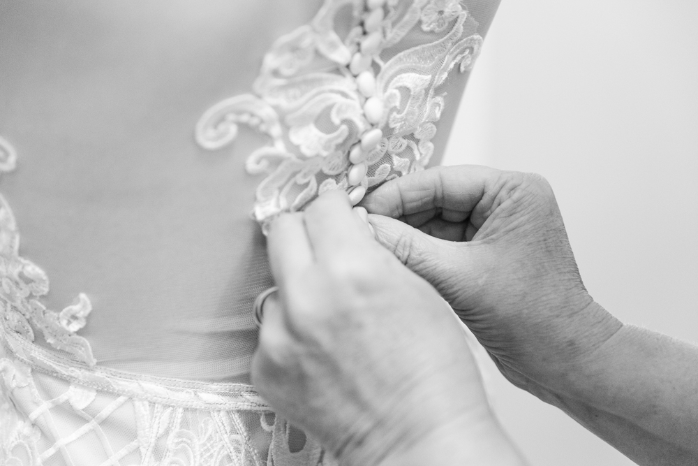 Someone buttoning back of lace wedding dress