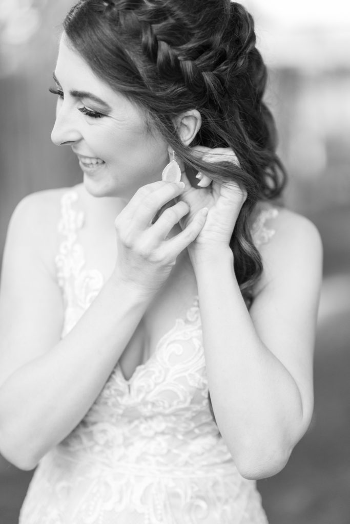 Bride putting on her teardrop crystal earring with a braid in her hair. 
