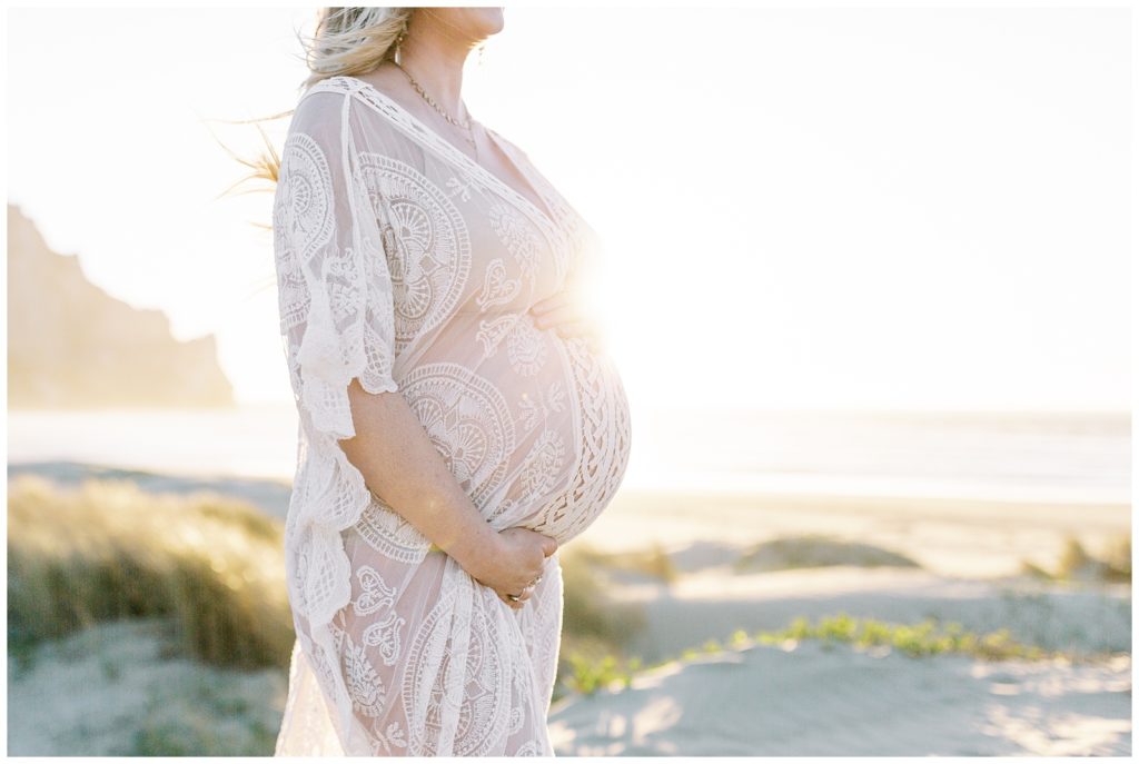 Woman's pregnant belly at sunset in boho sheer dress. 