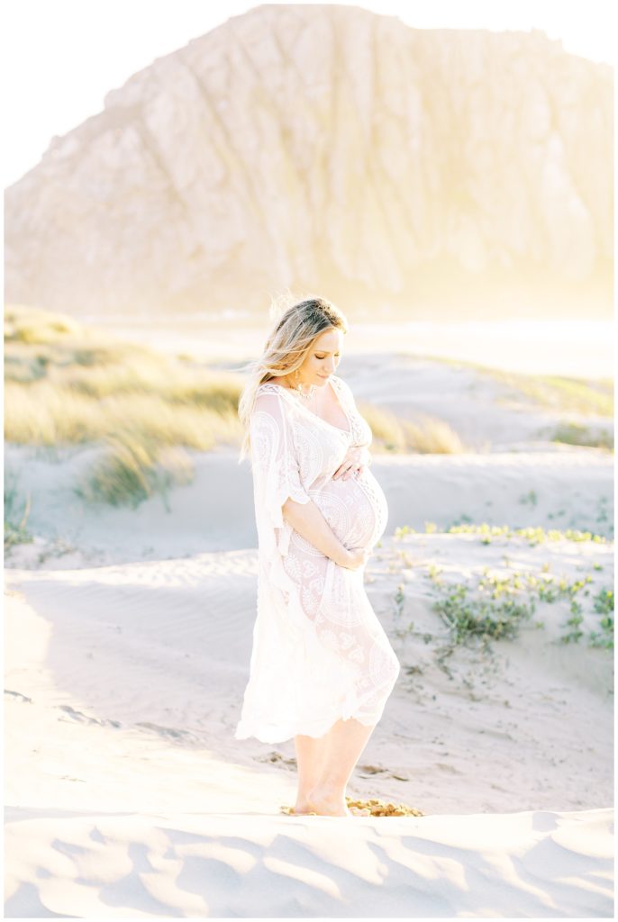 Woman looking at her pregnant belly in white boho maternity dress for beachy maternity photos