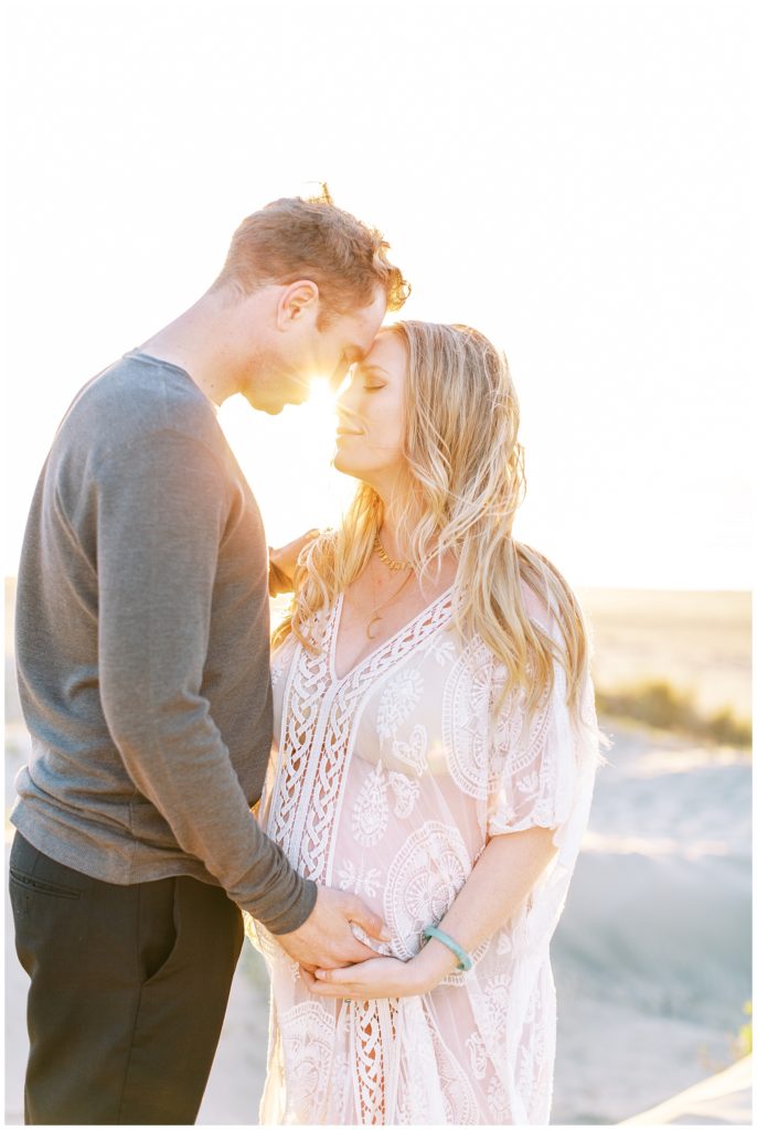 Couple touching foreheads and holding woman's pregnant belly at sunset