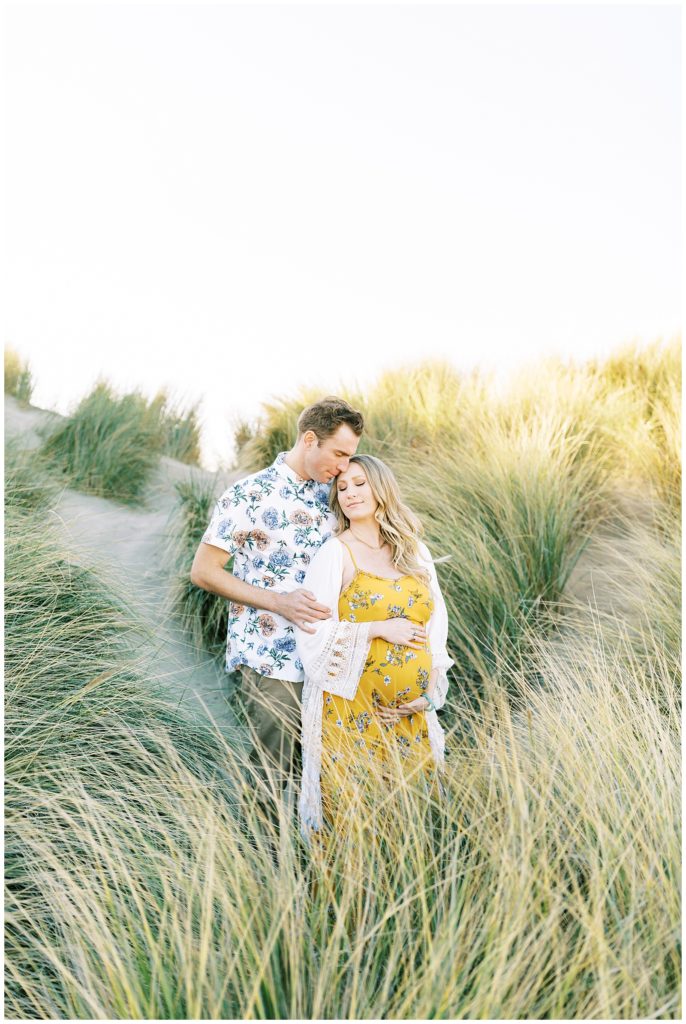 Maternity couple in the tall grass while woman holds her baby bump