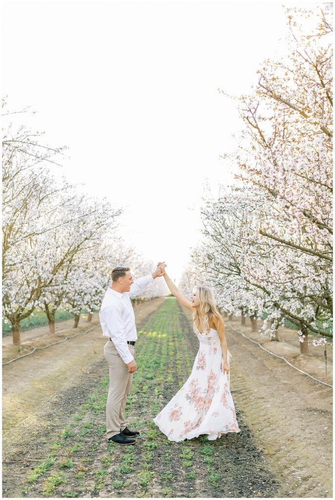spring engagement photos of a couple dancing in a blossom trail orchard