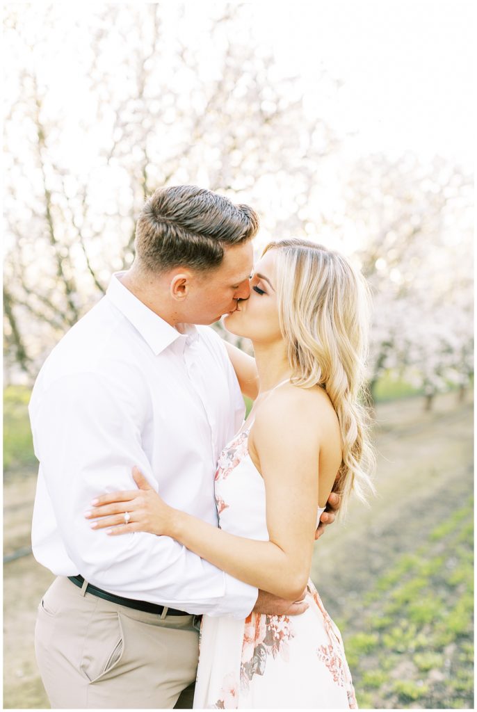 spring engagement photos of a couple kissing in the almond blossoms