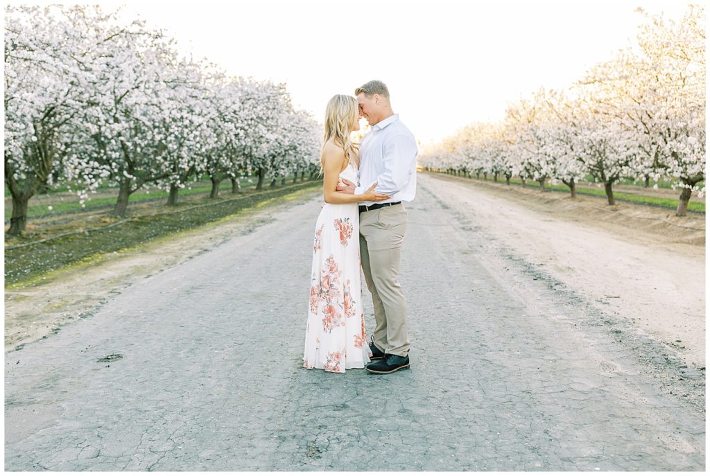 Couple standing touching foreheads in the road between white blossomed trees