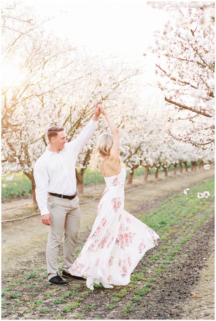 Film photo of man twirling his fiance in a floor length floral spring dress. 