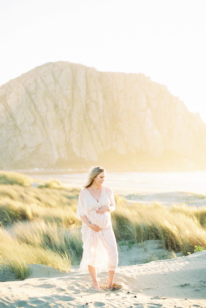 Film photo of woman in white boho dress at Morro bay holding baby bump