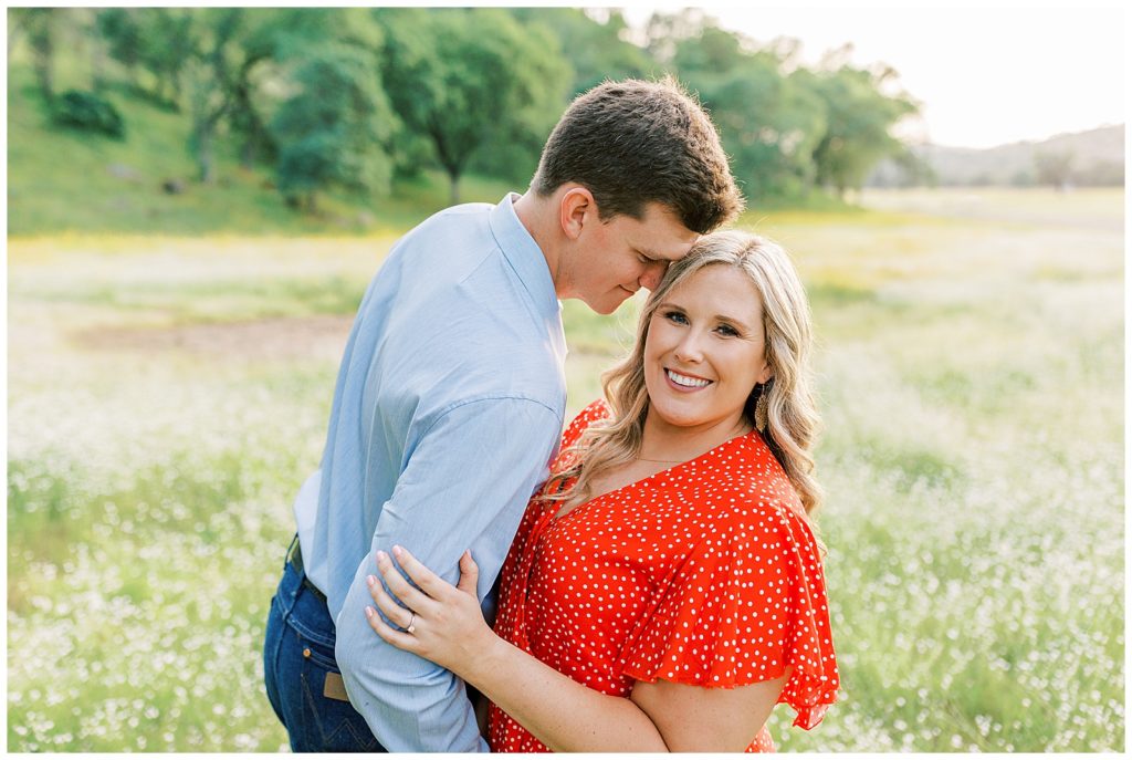 Man leaning in to womans temple while she smiles for engagement photos in wildflowers