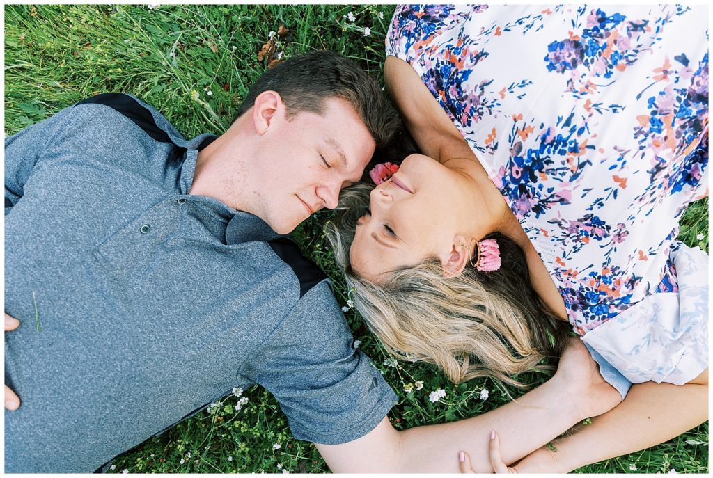 Couple laying in wildflowers head to head with their eyes closed. 