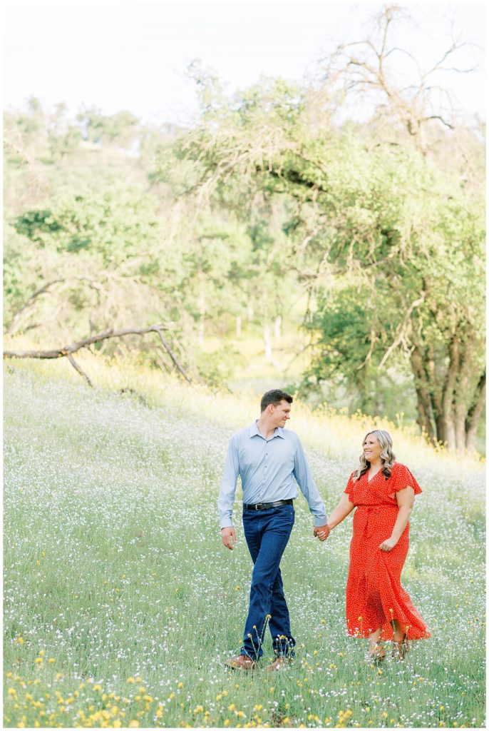 Man leading his fiance through a wildflower field for engagement photo.