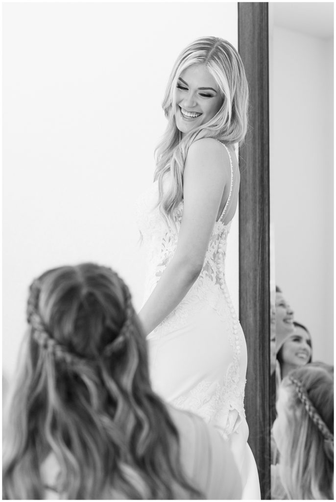 black and white photo of a bride smiling at her bridesmaids while getting ready