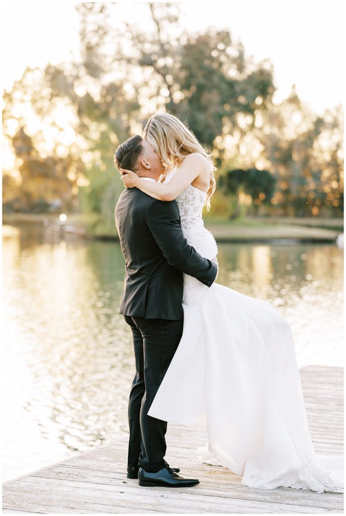 groom picking up bride and kissing her on a dock at wolf lakes park a fresno wedding venue