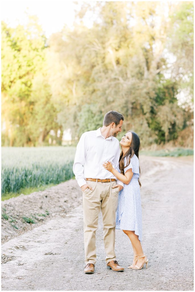 Spring engagement photo of woman in blue spring dress and man in tan slacks on a dirt road. 