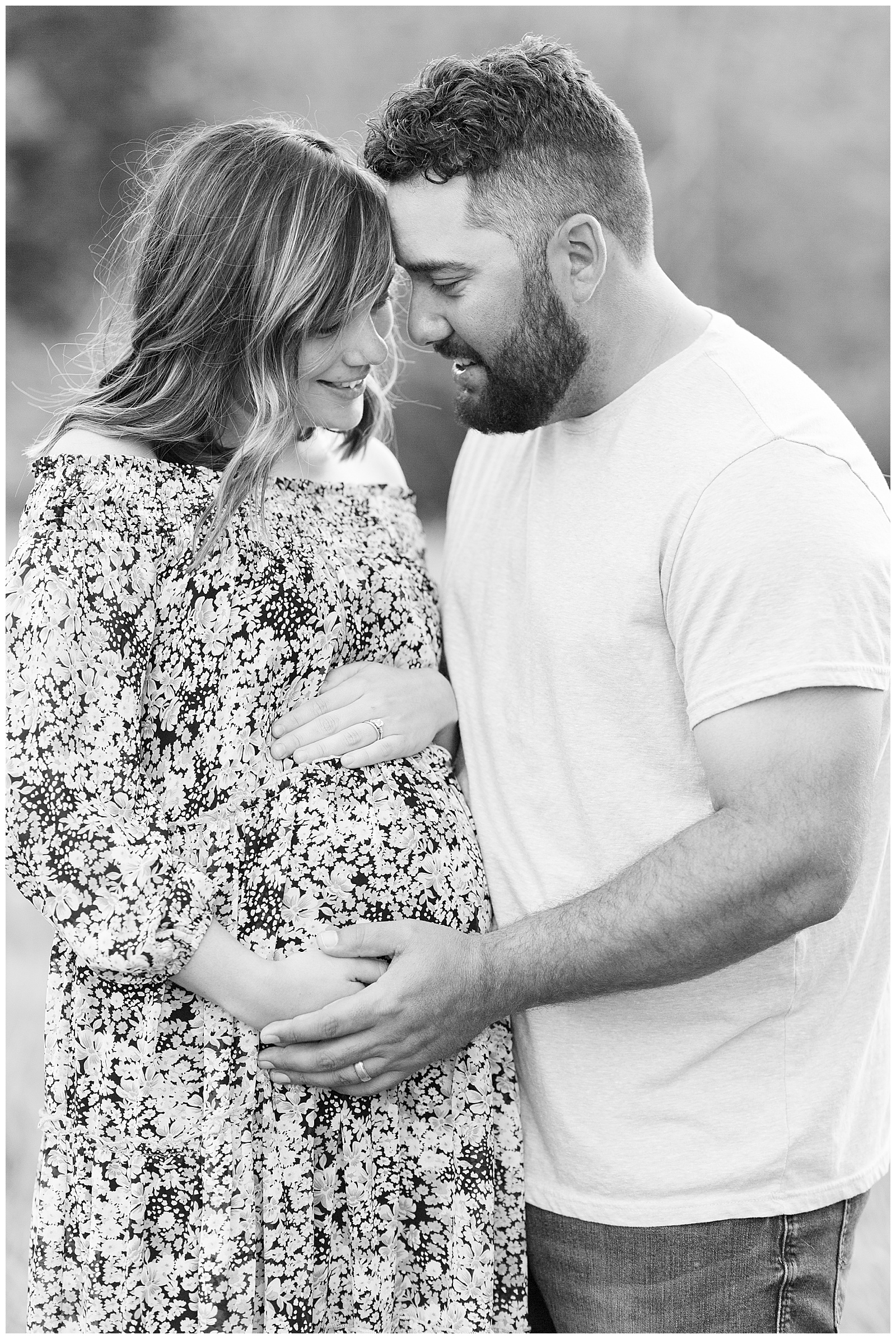 close up black and white photo husband and pregnant wife smiling and embracing 