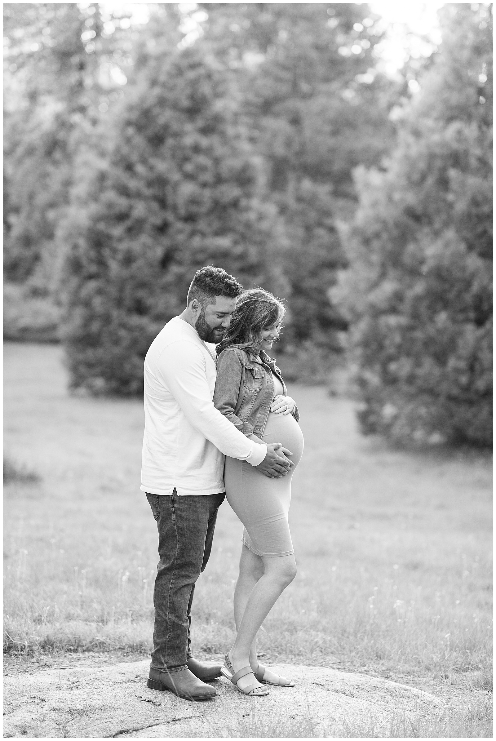 black and white photo of husband and pregnant wife looking at baby belly and smiling