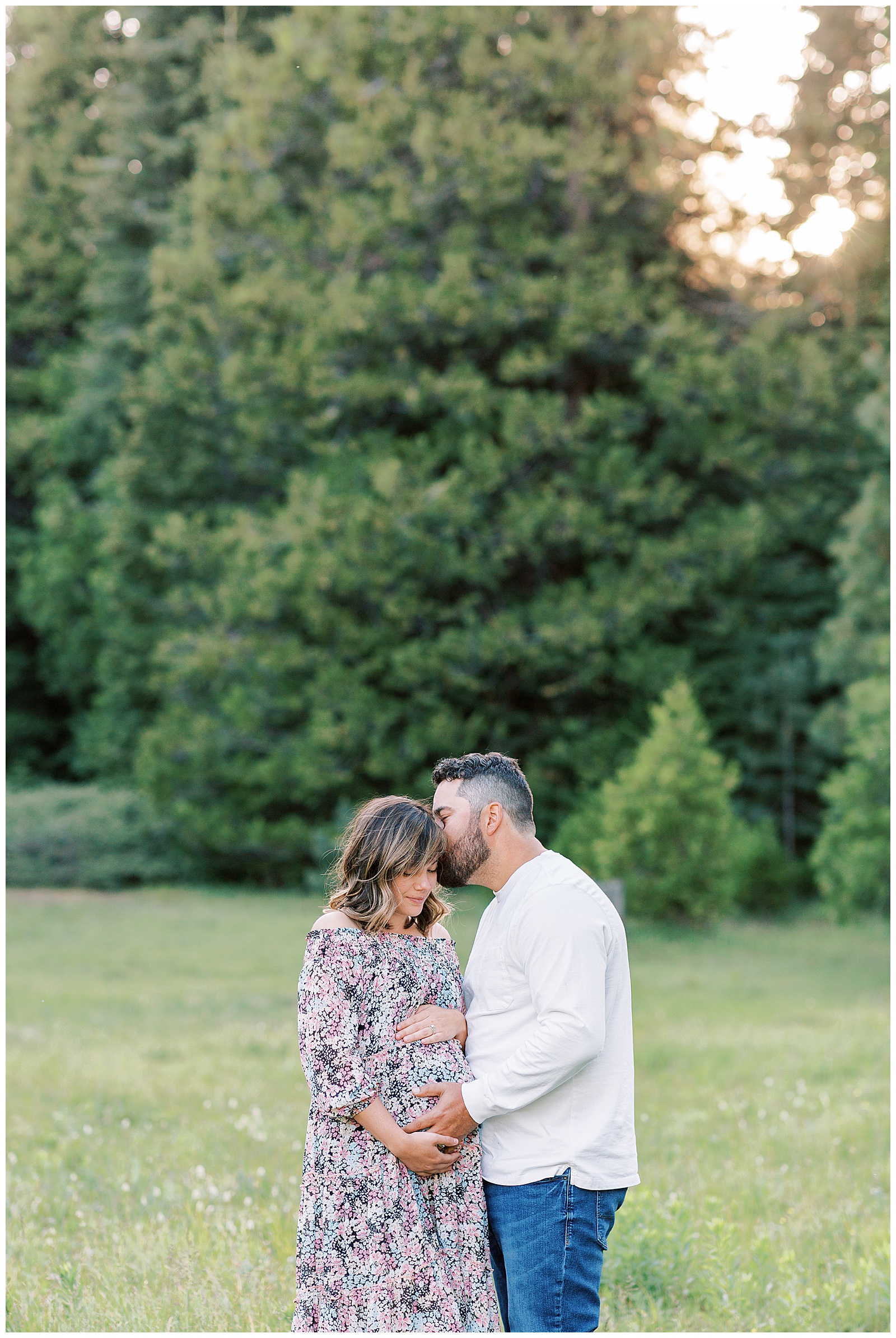 husband kissing wife at maternity photo session in meadow
