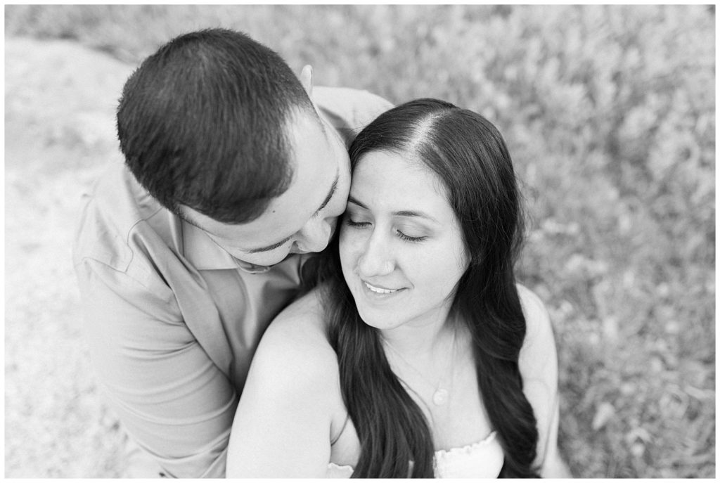 black and white photo of a couple sitting and him kissing her on the cheek