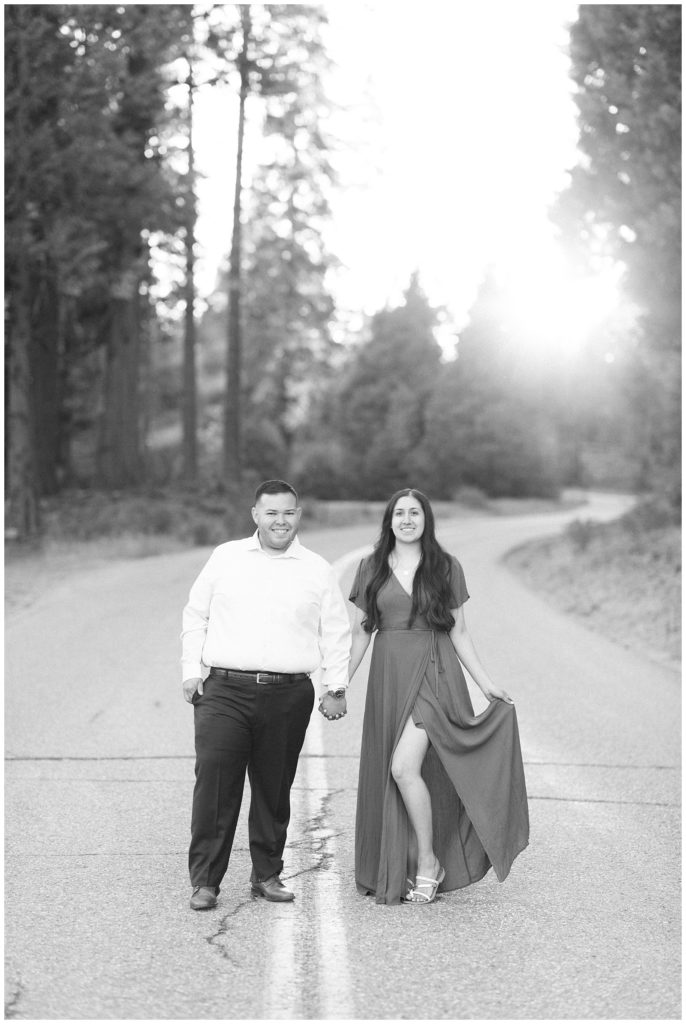 black and white photo of an engaged couple standing in the middle of a mountain road at sunset in shaver lake california