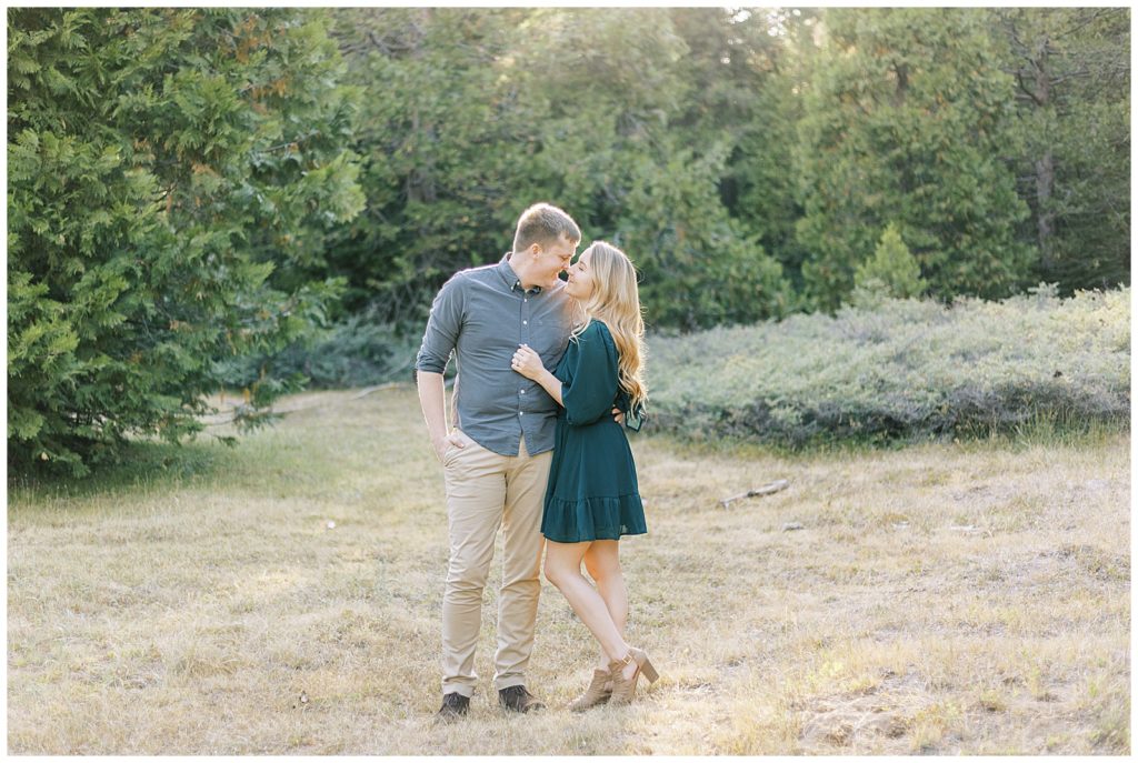 couple touching noses and embracing in a golden grassy mountain meadow with pine trees