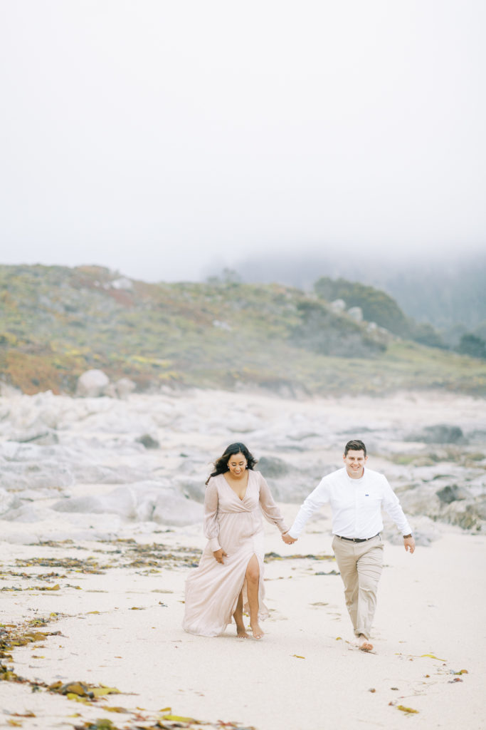 couple holding hands and walking along the shores of Carmel