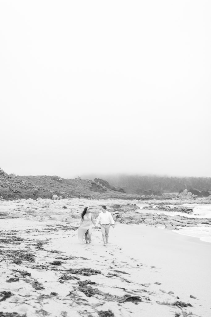 wide image of a couple walking along the beach in black and white