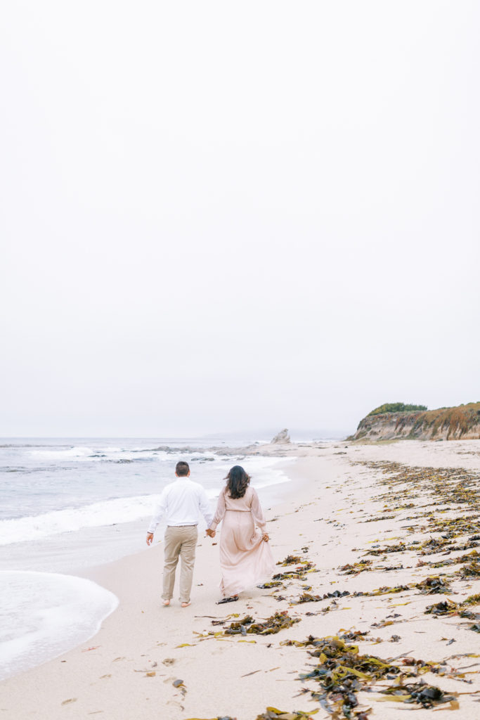 couple walking on the beach holding hands on a cloudy day in carmel by the sea california
