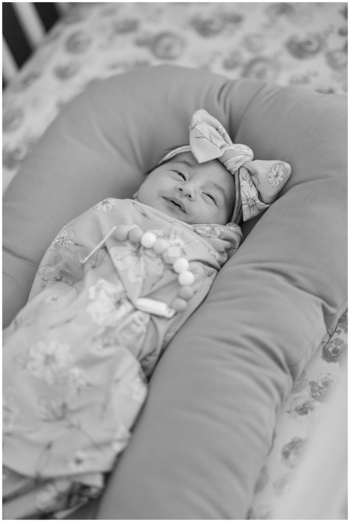 black and white photo of newborn baby girl swaddled and smiling