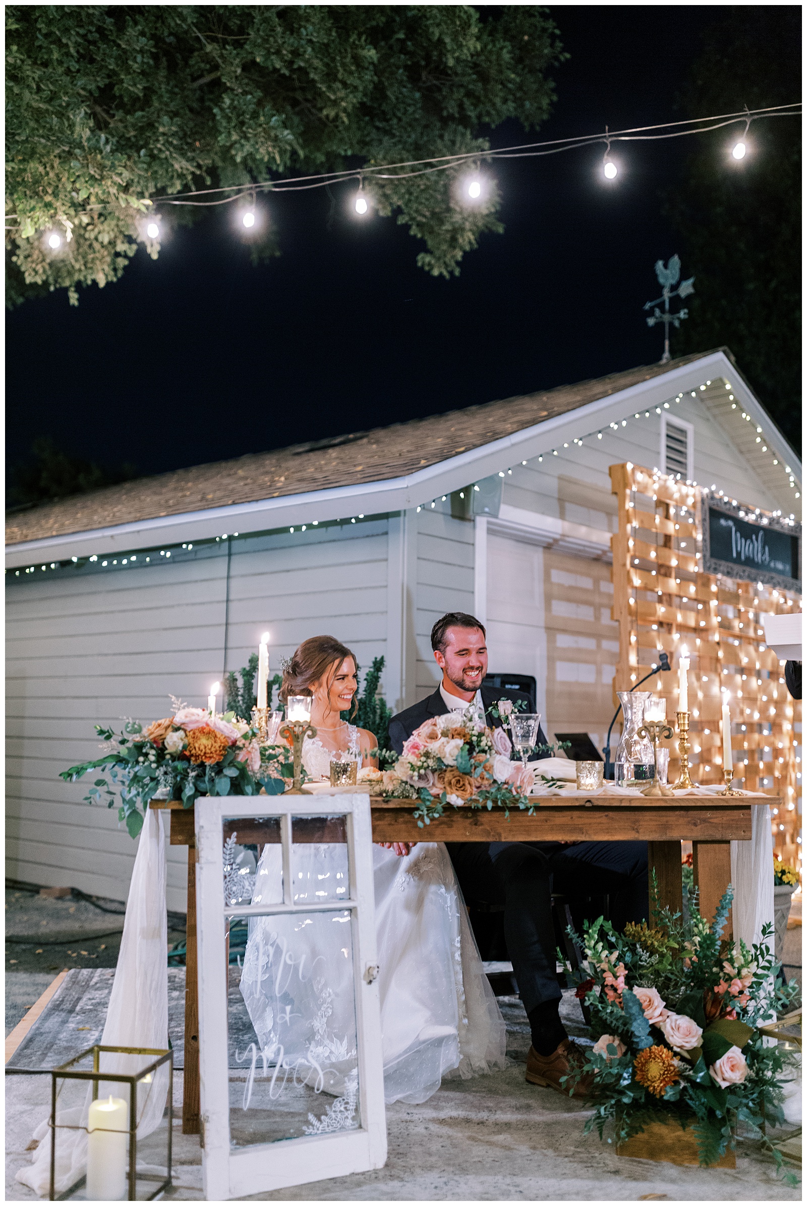 bride and groom sitting at sweetheart table smiling during toasts backyard wedding inspiration