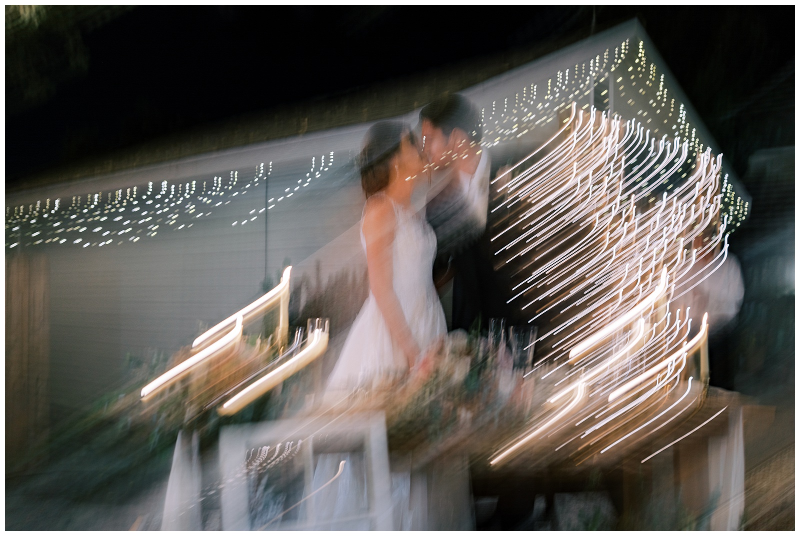 blurry image bride and groom kissing with lights in background