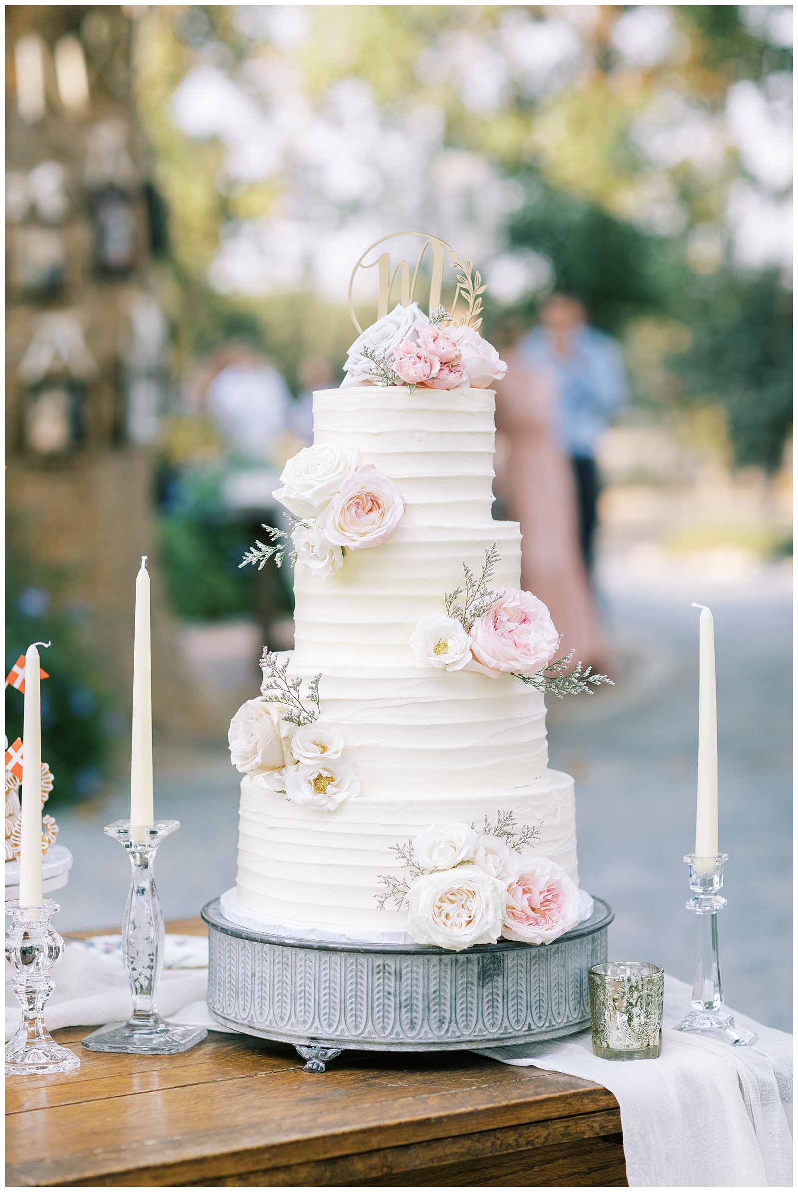 four tier wedding cake with white frosting and blush flowers with gold cake topper