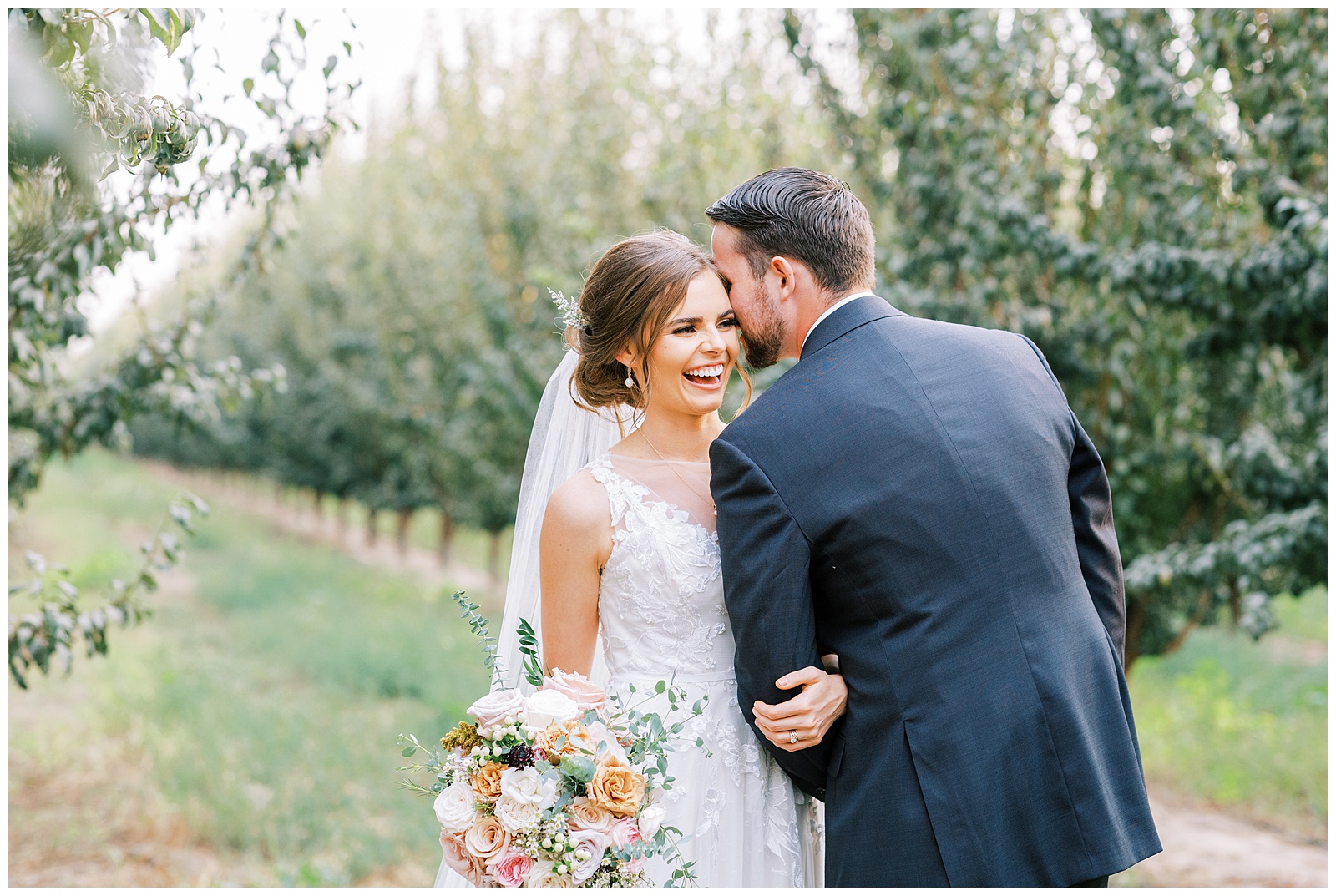 groom whispering in brides ear bride smiling in stone fruit orchard