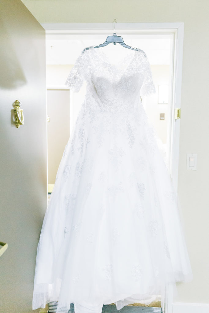 white wedding dress with lace sleeves hanging in doorway