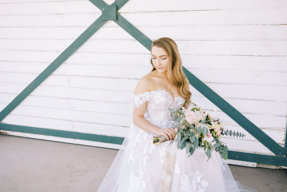 bride sitting in front of white barn doors holding pink and white wedding bouquet