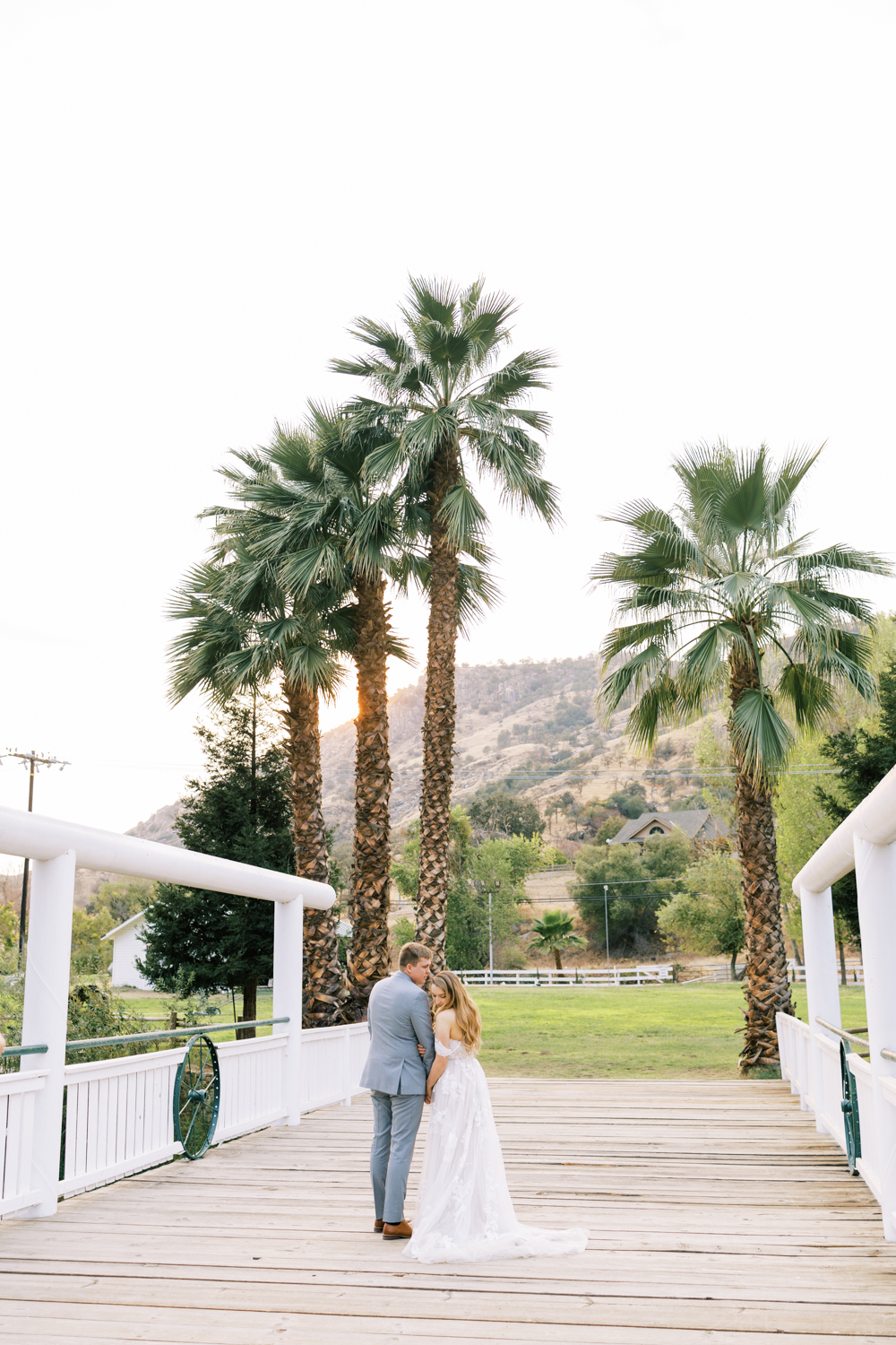 bride and groom holding hands palm trees and sunset behind them at springville ranch