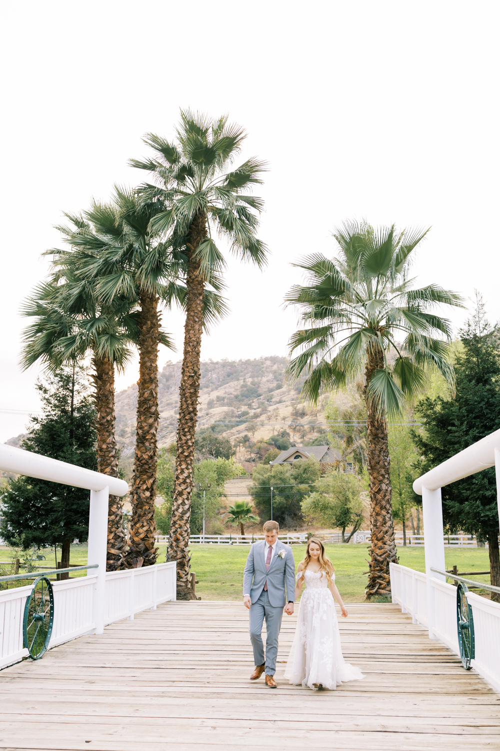 bride and groom holding hands walking along a bridge palm trees in background