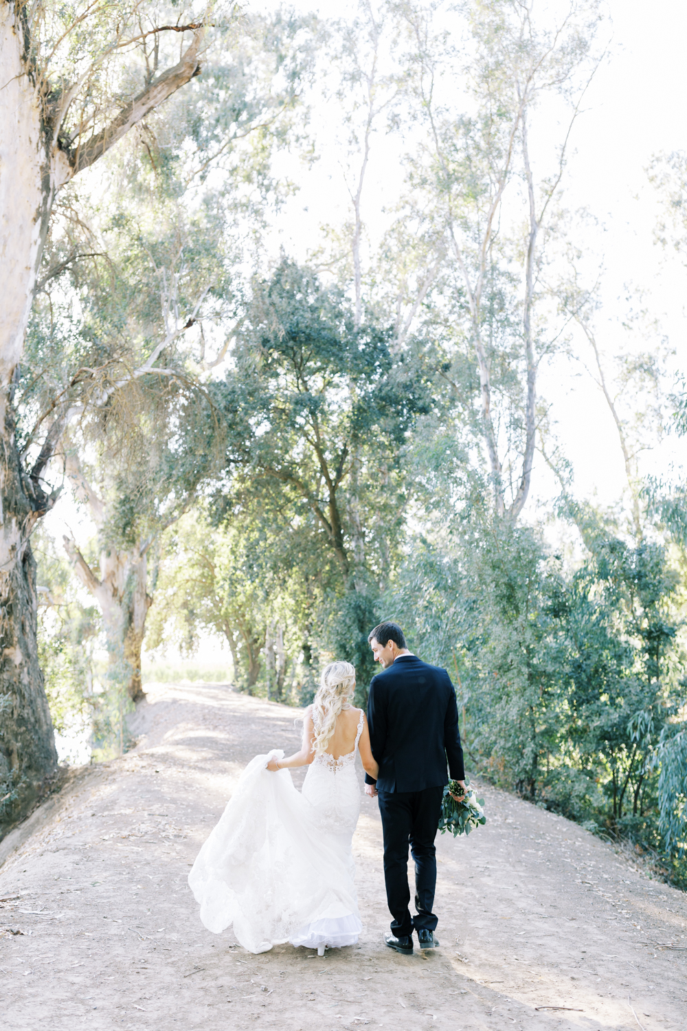 bride and groom holding hands and walking away down a eucalyptus lines drive