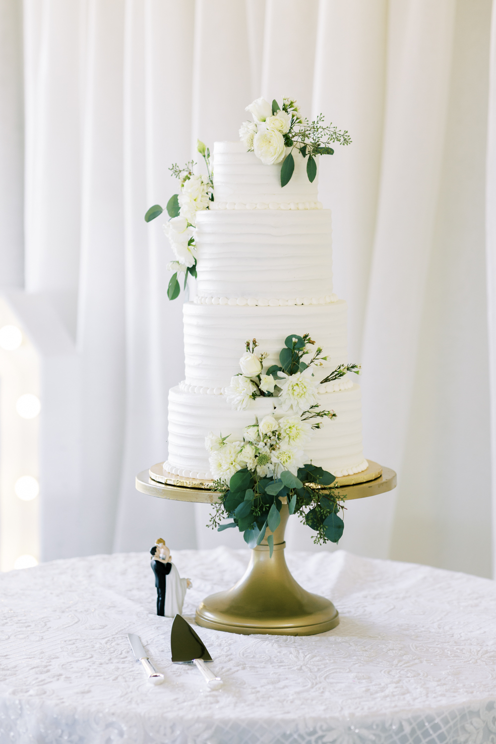 white four tier wedding cake with white roses and eucalyptus details 
