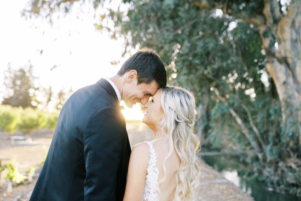 bride and groom touching noses and smiling with sunset behind them