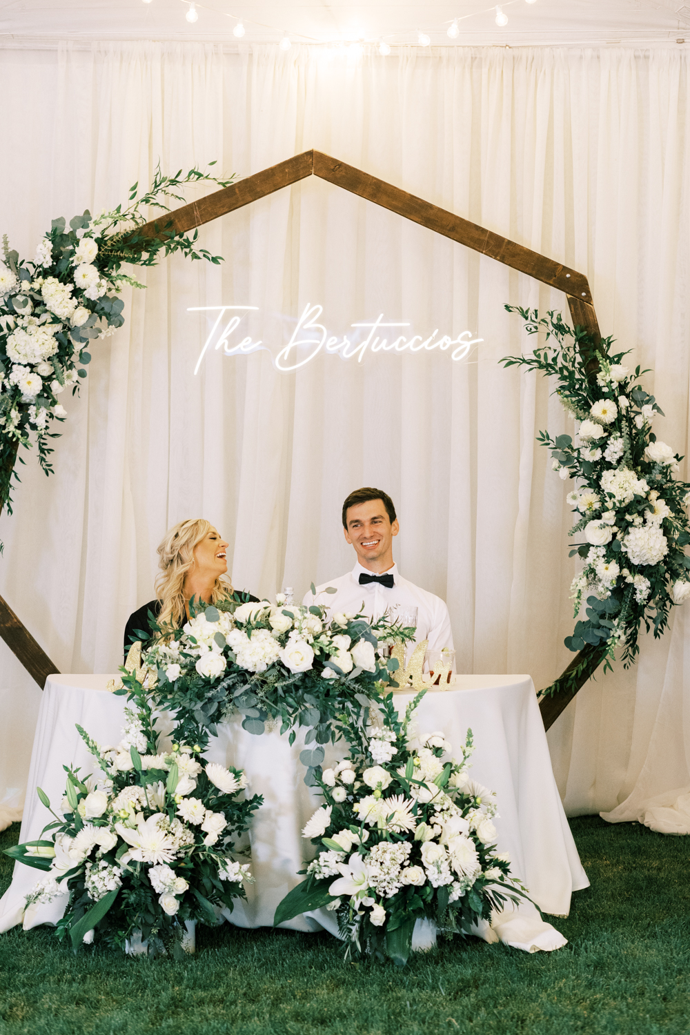 bride and groom sitting at head table with hexagon arch smiling at elegant backyard wedding during wedding reception