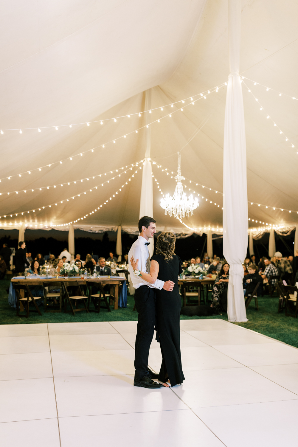 groom dancing with his mother under white tent at wedding reception