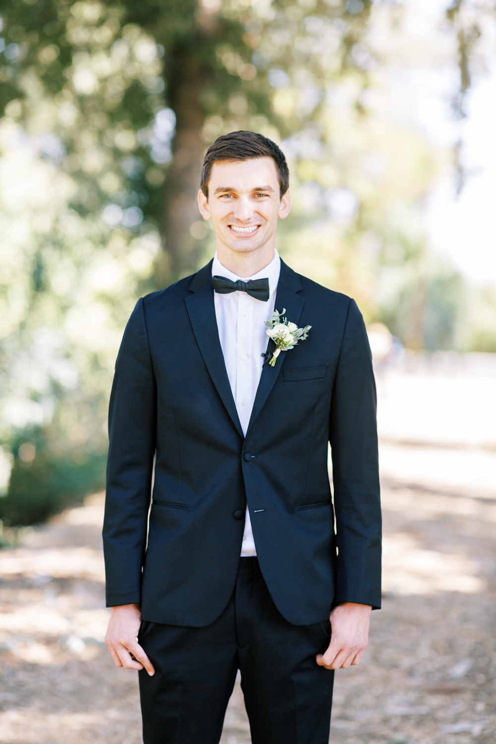 groom in black suit with bow tie smiling