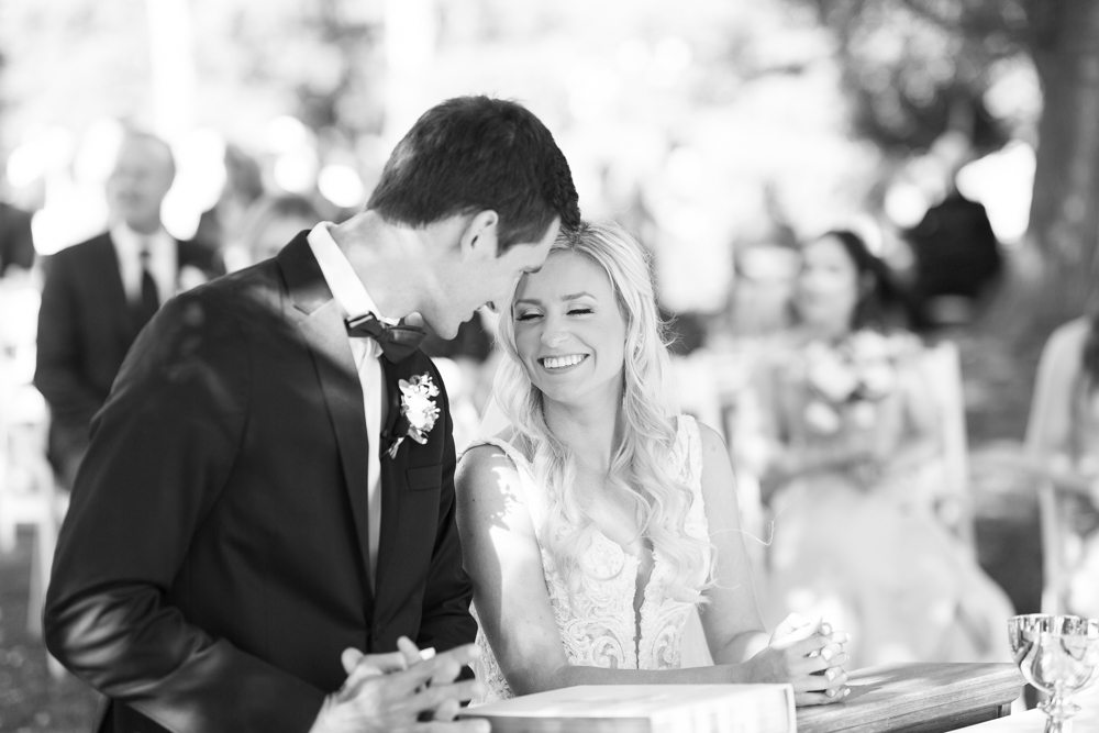 black and white photo of bride and groom smiling at each other at altar catholic wedding ceremony outdoors