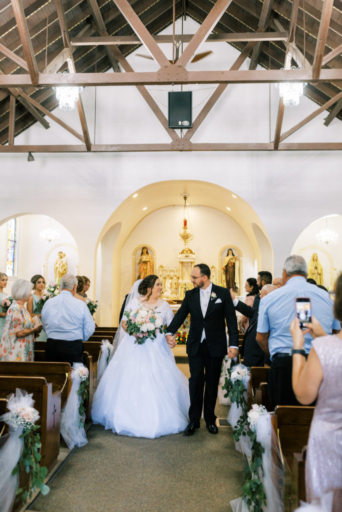 bride and groom holding hands walking down aisle after wedding ceremony in catholic church