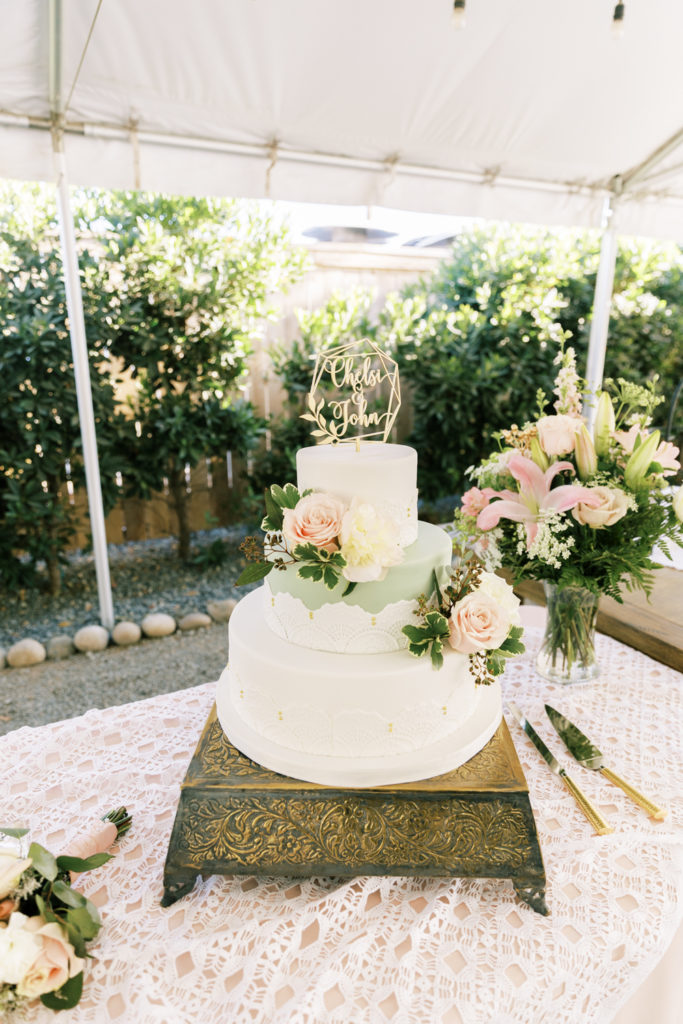 white and sage green wedding cake with gold cake topper and blush florals