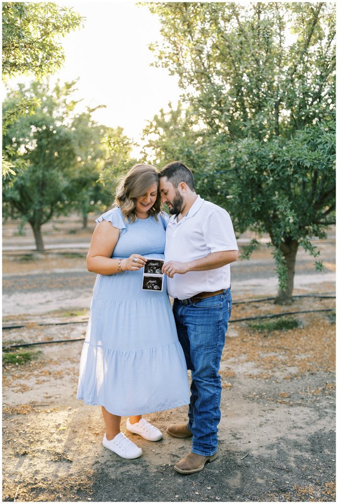 husband and wife holding sonogram photo in almond orchard