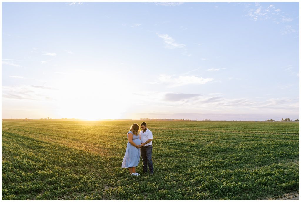 husband and wife standing in alfalfa field at sunset summer maternity photos
