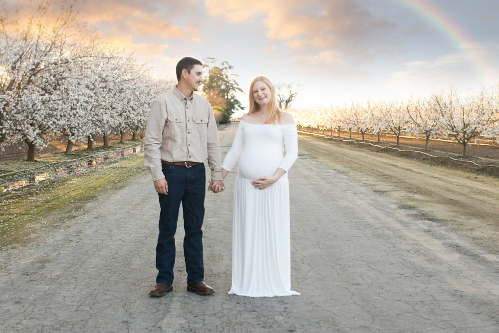 sunset photo with a rainbow in the sky of a couple during a maternity session along the blossom trail