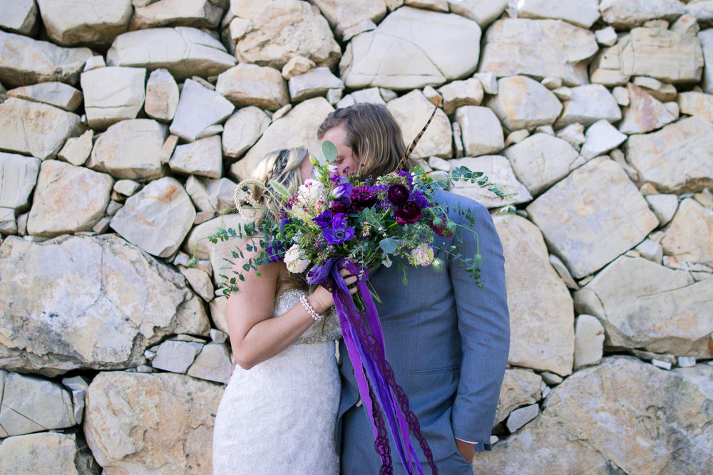 bride and groom kissing behind a lavender wedding boquet