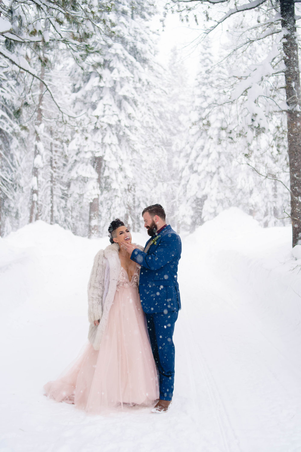 candid portrait of a bride and groom in the snow while the snow falls